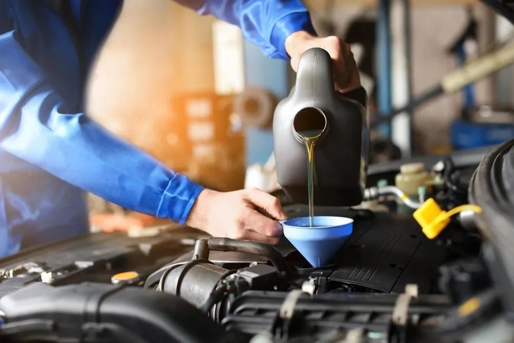 Männlicher Mechaniker beim Nachfüllen von Autoöl im Servicecenter