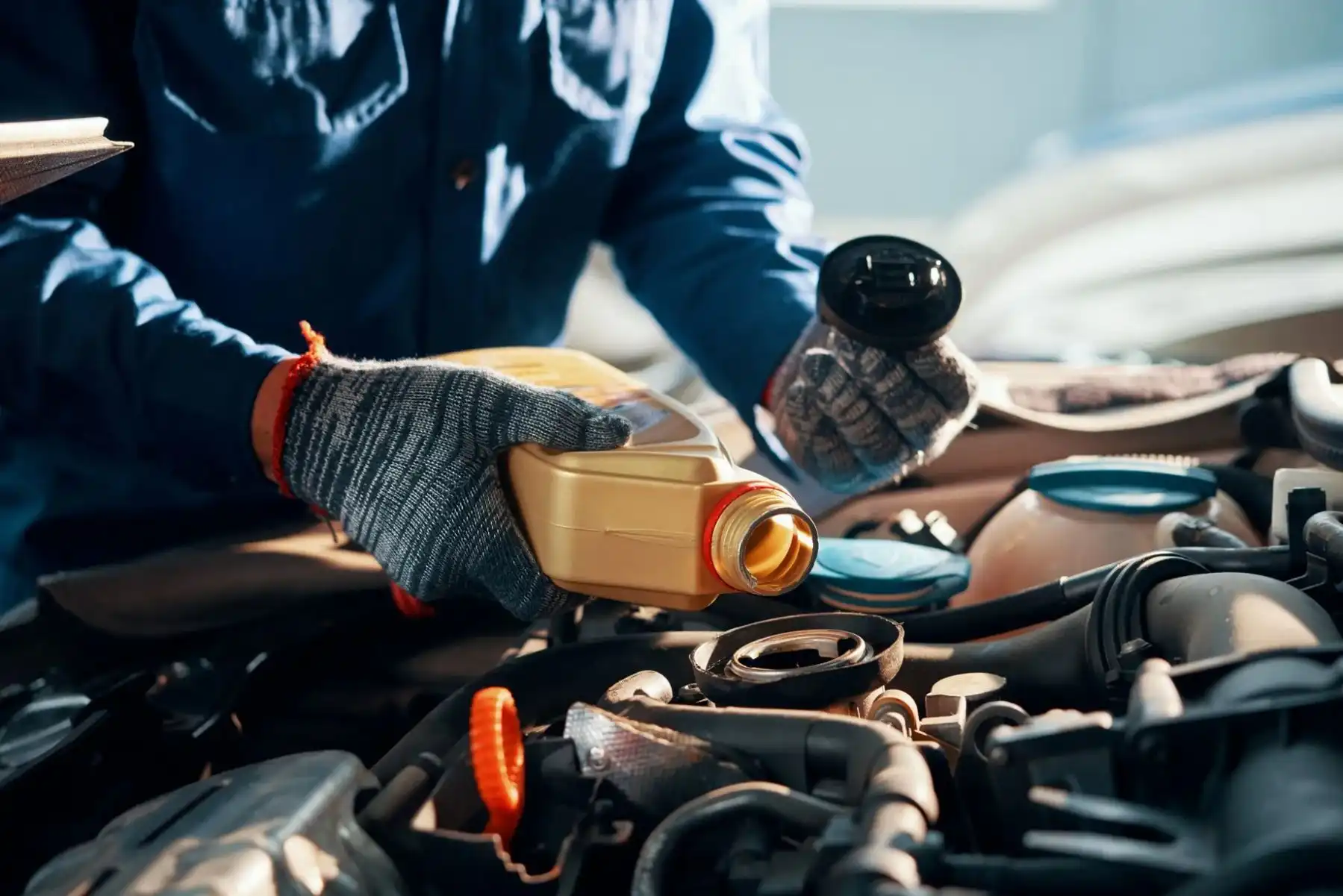 Hände eines Mechanikers, der eine Flasche Öl in einen Automotor gießt